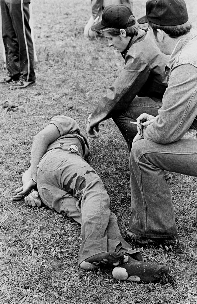The Missouri Water Patrol sharpshooter (center) kneels at a fugitive's side minutes after felling him with a single shot from across a field.